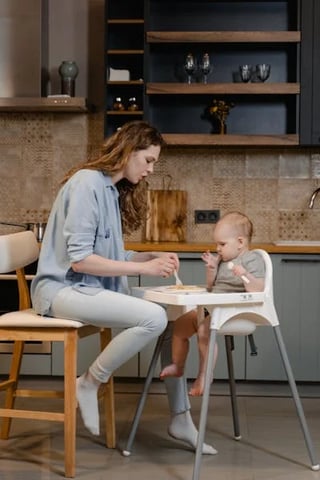 A mother feeding her baby in a high chair, introducing solid foods in a cozy kitchen setting.