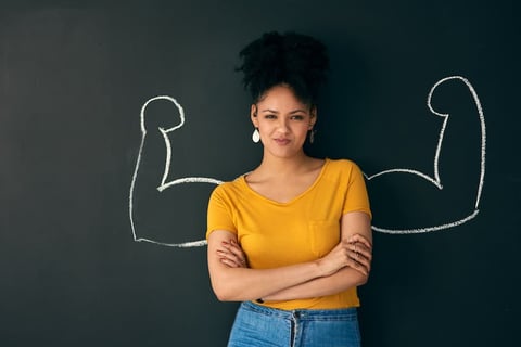 A woman with arms crossed in front of a blackboard.