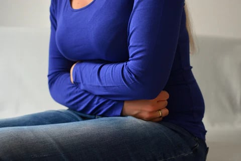 Woman sitting and holding her stomach.