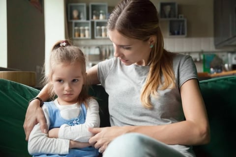 A woman on a green couch next to her sullen small daughter.