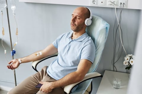 A reclining man in headphones, eyes closed, with an IV drip on his arm.