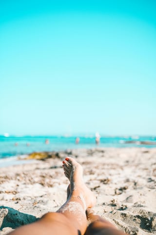 Person relaxing on a beach with sandy feet, gazing towards the blue ocean.