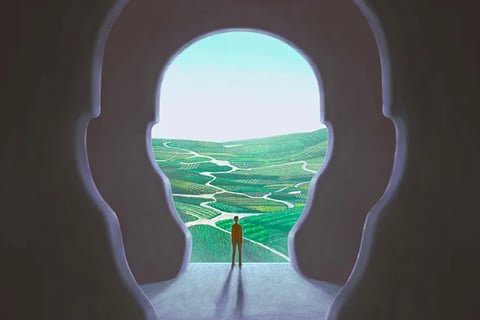 An illustration of a man standing in a cave shaped like a head looking over a green valley below.