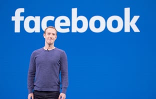 Mark Zuckerberg stands in front of the Facebook logo. Photo: Creative Commons