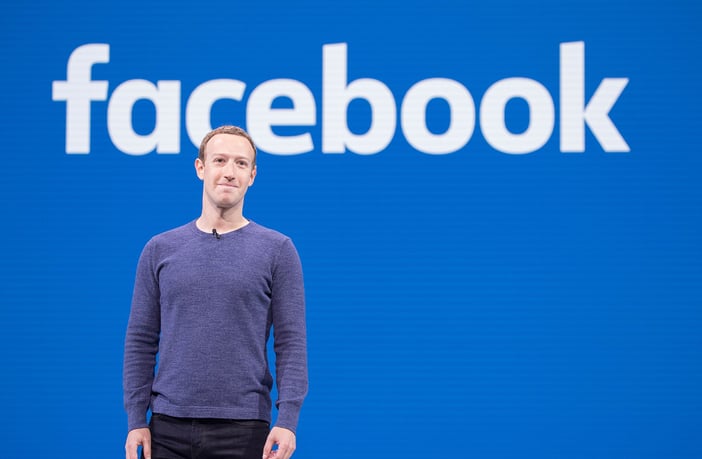 Mark Zuckerberg stands in front of the Facebook logo. Photo: Creative Commons