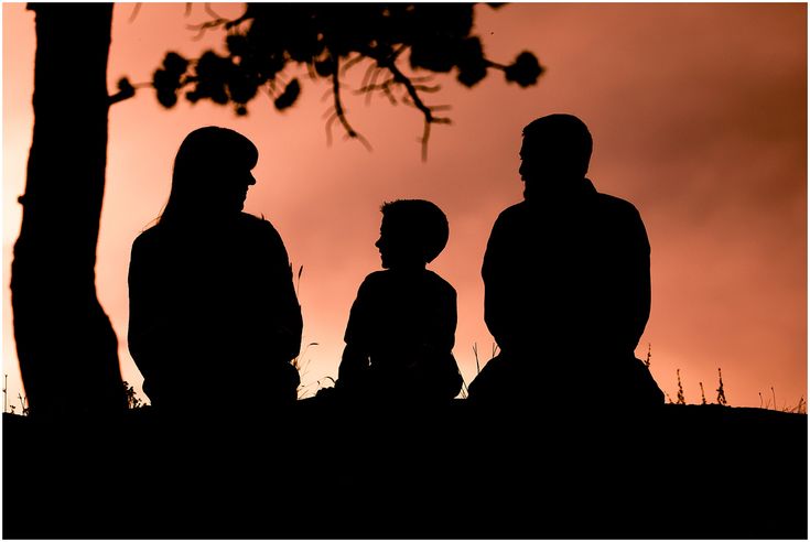 A happy family standing together under the warm hues of a beautiful sunset, creating a silhouette against the sky, capturing the essence of togetherness and serenity.