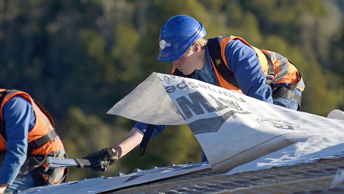 Roofers in safety gear installing roofing underlay on a residential building