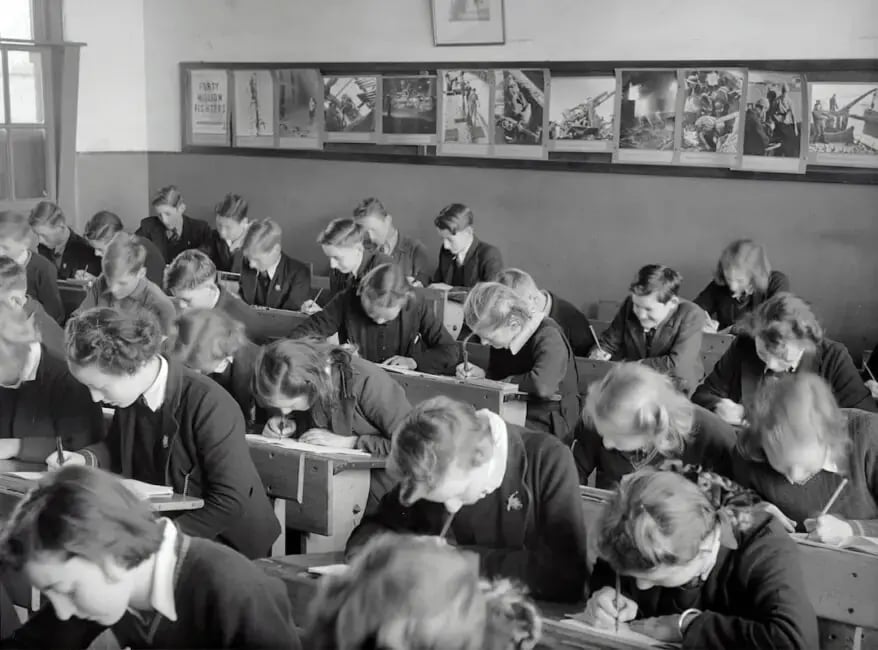 A black and white photo of a classroom with many students sitting at desks.