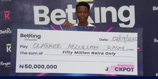 An image of Olatunde Abdullah, BetKing's Virtuals Jackpot winner beaming while holding his prize cheque money