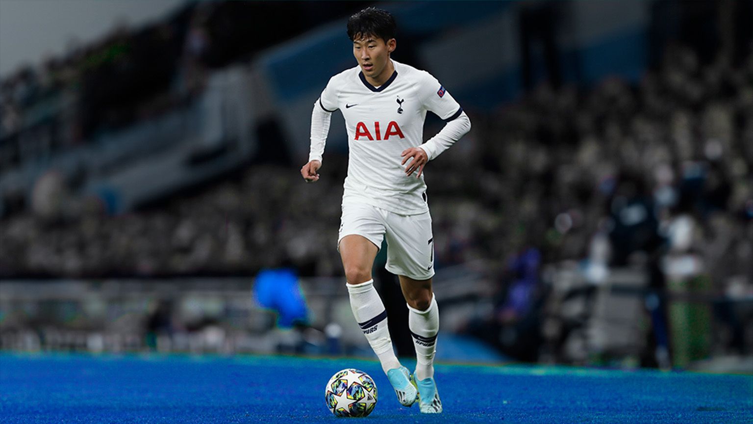 Heung Min Son advancing a milticolored (but mostly white) ball. He's wearing a white Tottenham jersey with "AIA" in bold red font