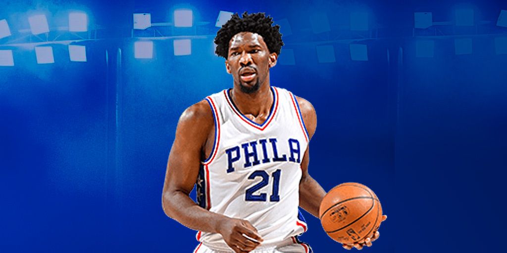 Joel Embiid wearing a Philly 76ers jersey and palming an orange basketball