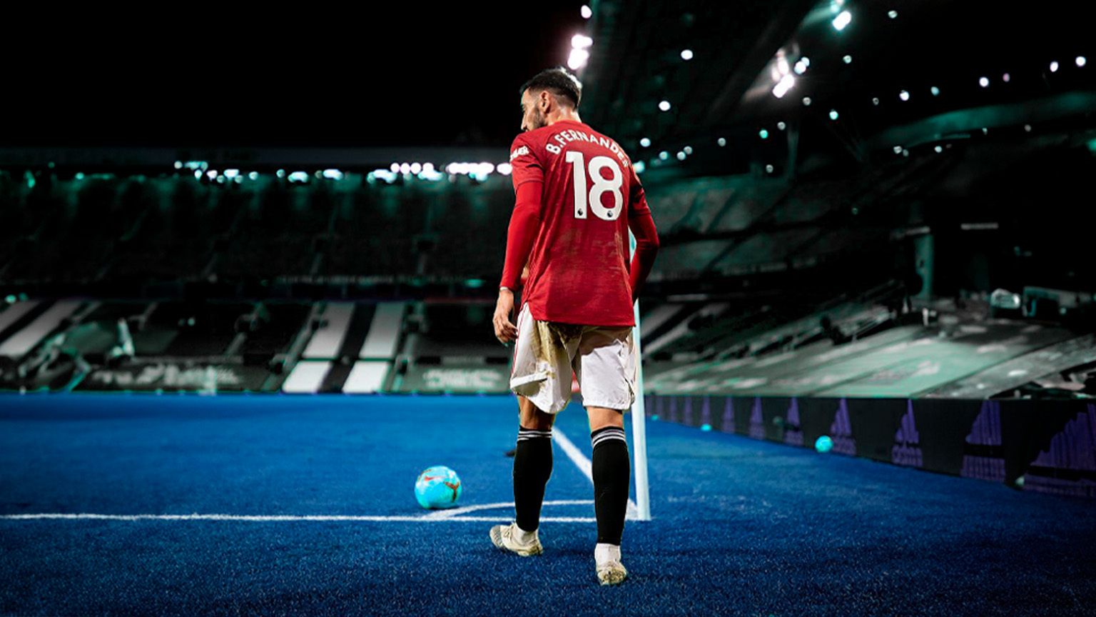 Bruno Fernandes taking a corner. In the image, he's wearing a red Manchester United flag and standing by the corner flag with the stadium stretching off into the background