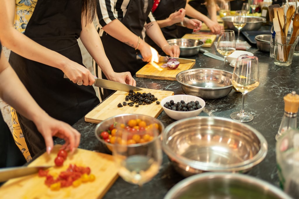 Personas preparando ingredientes en una clase de cocina, cortando verduras en una mesa con tazones y vasos.