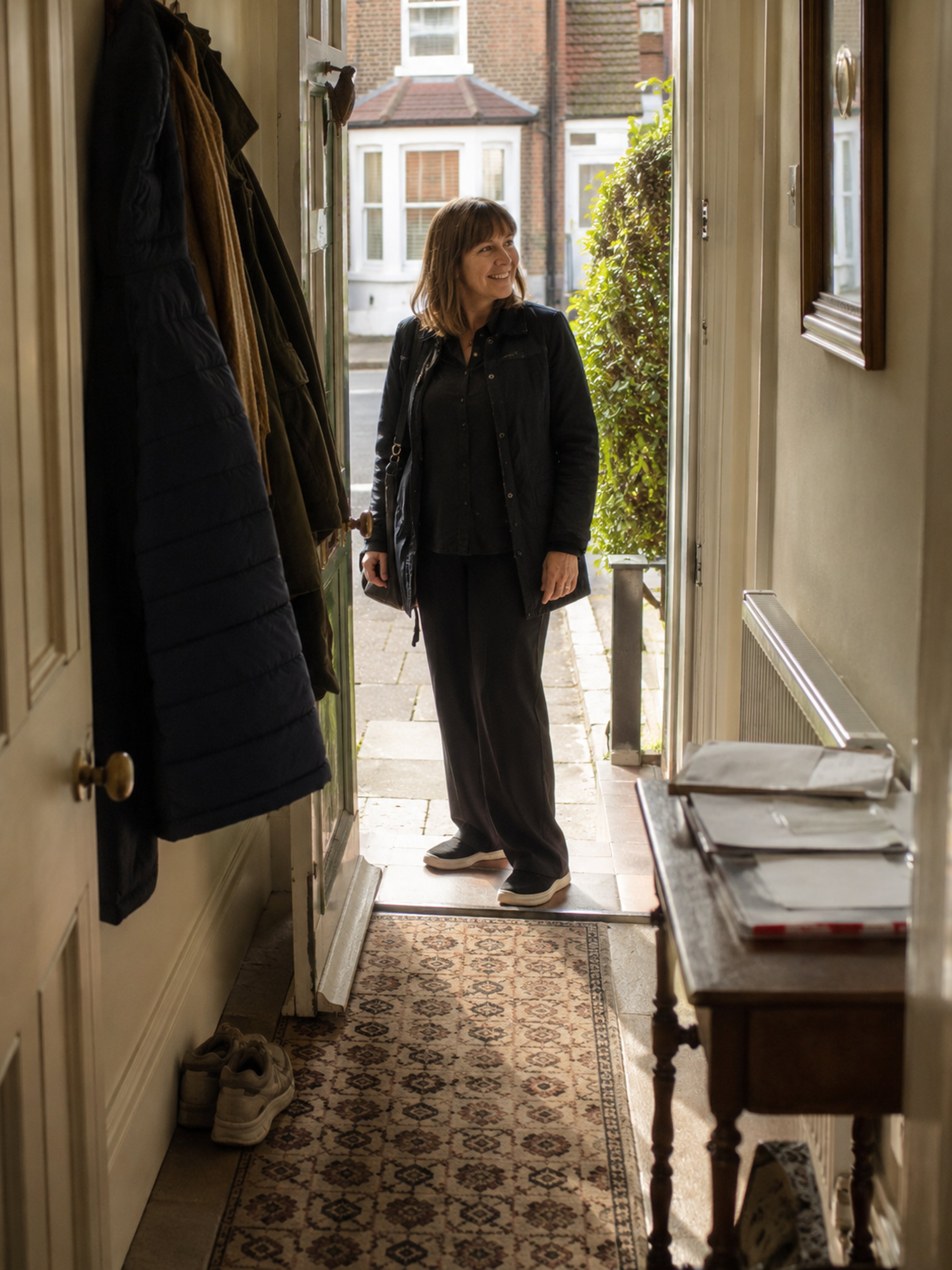 A carer welcomed in at a front door, seen from inside the hall. Not a uniform shot.