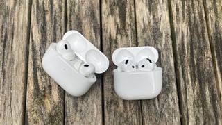 AirPods 4 și AirPods Pro 2 alăturate în carcasele lor de încărcare pe o suprafață de lemn.