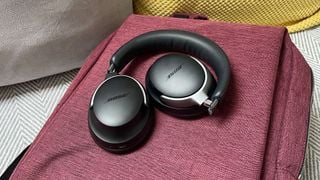 O pereche neagră de căști Bose QuietComfort Ultra pliate pe o geantă roșie.