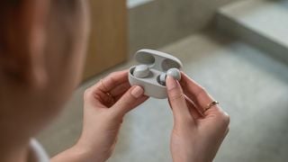 Imagine lifestyle Sony WF-1000XM5 arătând o femeie care scoate o cască din carcasa de încărcare