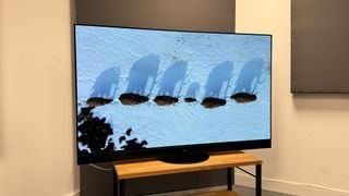 Televizorul Panasonic MZ2000 pe un suport TV, cu o linie de elefanți văzută de sus pe ecran.