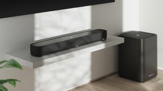 Soundbar și subwoofer poziționate sub un televizor montat pe perete