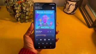 Samsung Galaxy S22 Plus ținut în fața unei suprafețe galbene. Pe ecran este 'Heat Waves' de Glass Animals pe Tidal.