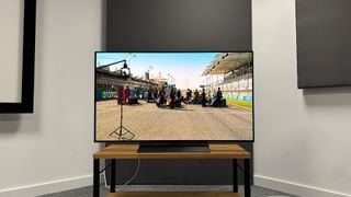 Televizor LG C4 (OLED48C4) vedere frontală în colțul unei camere de test cu cursă F1 pe ecran