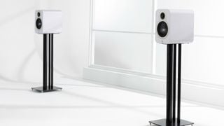 Boxe Q Acoustics 3020c albe pe suporturi într-o cameră minimalistă