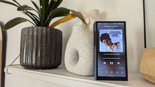 Player de muzică portabil Fiio M23 vertical pe raft alb lângă o plantă de casă
