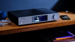 Streamer Cambridge Audio CXN100 cu aplicație pentru smartphone pe un raft din lemn
