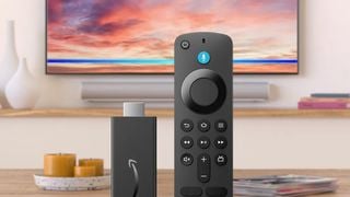 Amazon Fire TV Stick HD și telecomanda Alexa cu un televizor și o bară de sunet în fundal.