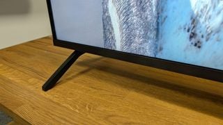Televizor Panasonic W90A de 65 de inch arătând piciorul și partea de jos a ecranului pe o suprafață de lemn