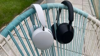 Căști over-ear Sonos Ace albe și Sony WH-1000XM5 negre, atârnând pe spatele unui scaun.