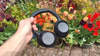 Căștile Sony ULT Wear over-ear în mână, pe un fundal de flori