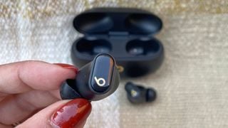 Un singur earbud Beats Studio Buds Plus ținut între degetul mare și arătător