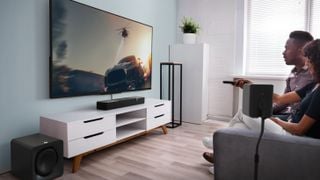 Soundbar Klipsch Flexus, subwoofer și difuzor într-o sufragerie modernă cu un televizor mare montat pe perete și unitate media albă