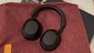 O pereche neagră de căști Sony WH-1000XM5 pe o geantă roșie.