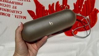 Boxă Bluetooth Beats Pill ținută în mână pe un fundal grafic roșu și alb