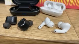 Cambridge Audio Melomania M100 vs AirPods Pro 2 cu carcasele lor de încărcare pe o masă de lemn
