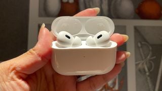 O pereche de Apple AirPods Pro 2 în carcasa de încărcare, ținută de o mână.