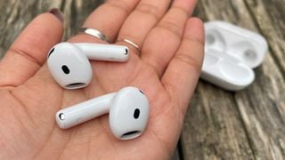 Căști wireless Apple AirPods 4 cu ANC ținute în palma mâinii deasupra unei mese de lemn