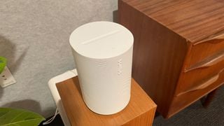 Boxa Sonos Era 100 în finisaj alb pe o bază de lemn într-un cadru de living