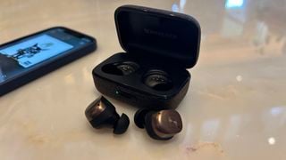 Căștile Sennheiser Momentum True Wireless 4 scoase din carcasă, lângă un telefon