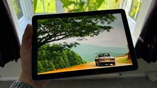 Tableta Amazon Fire HD 10 (2023) ținută în mână în fața unei ferestre cu mașină și copaci pe ecran