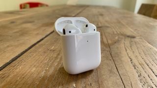 Apple AirPods (2019) în carcasa lor de încărcare pe o masă de lemn