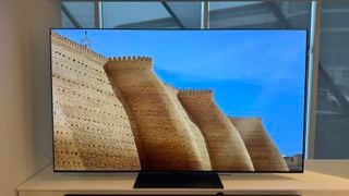 Televizorul LG G4 OLED fotografiat pe un suport alb într-un showroom, cu o bară de sunet poziționată în față