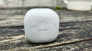 Carcasa de încărcare pentru căștile intraauriculare Sony LinkBuds Fit pe masă de lemn în aer liber