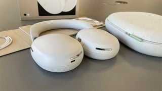 Căști Sonos Ace cu anulare a zgomotului întinse plat lângă carcasă pe suprafață gri