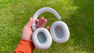 Căști Sonos Ace cu anulare a zgomotului ținute în mână arătând interiorul cupolelor pe fundal de iarbă