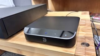 Streamer muzical Bluesound Node Nano pe masă de lemn, vedere din față/lateral