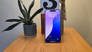 Smartphone Apple iPhone 16 așezat pe masă de lemn lângă o plantă în ghiveci