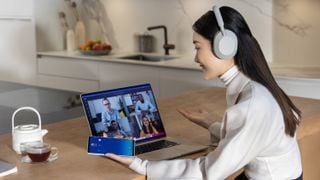 Fată purtând Sony WH-1000XM5, ținând un telefon și uitându-se la un laptop